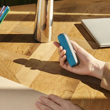Hand Holding a Ploom AURA device with an Ocean Blue Back Cover accessory