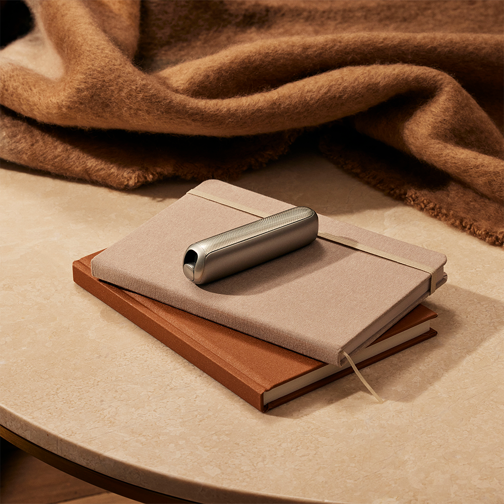 Ploom AURA front panels with Lunar Silver Augmented Pattern placed on top of a stack of notebooks.