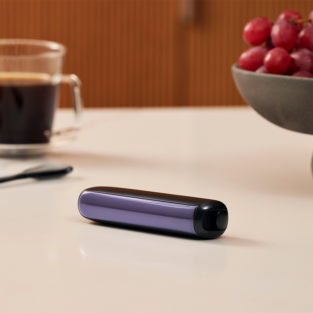 Ploom AURA front panel Lavender device stored on table.