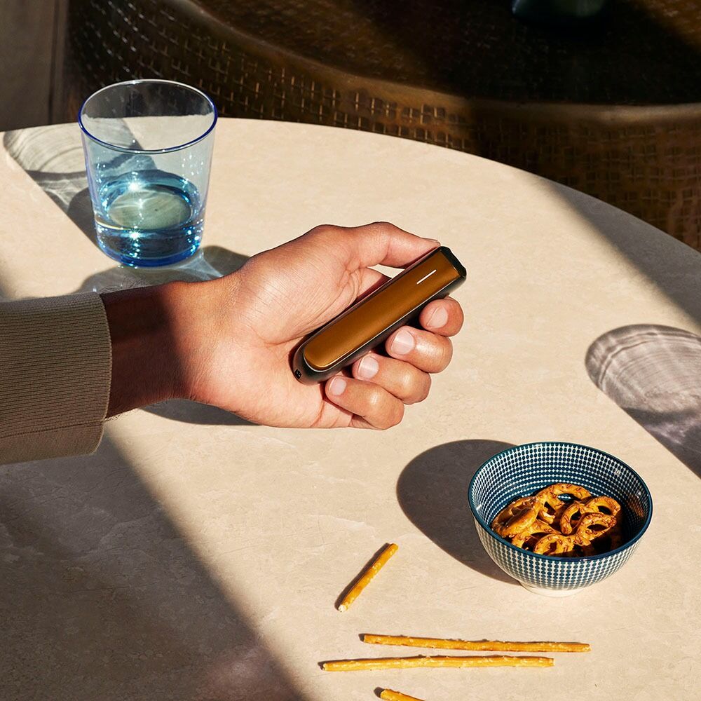 Hand holding Ploom AURA equiped with Mango Sorbet front panel.