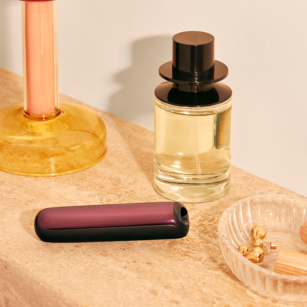 Ploom AURA front panel Dark Orchid accessory attached to device on a dressing table.